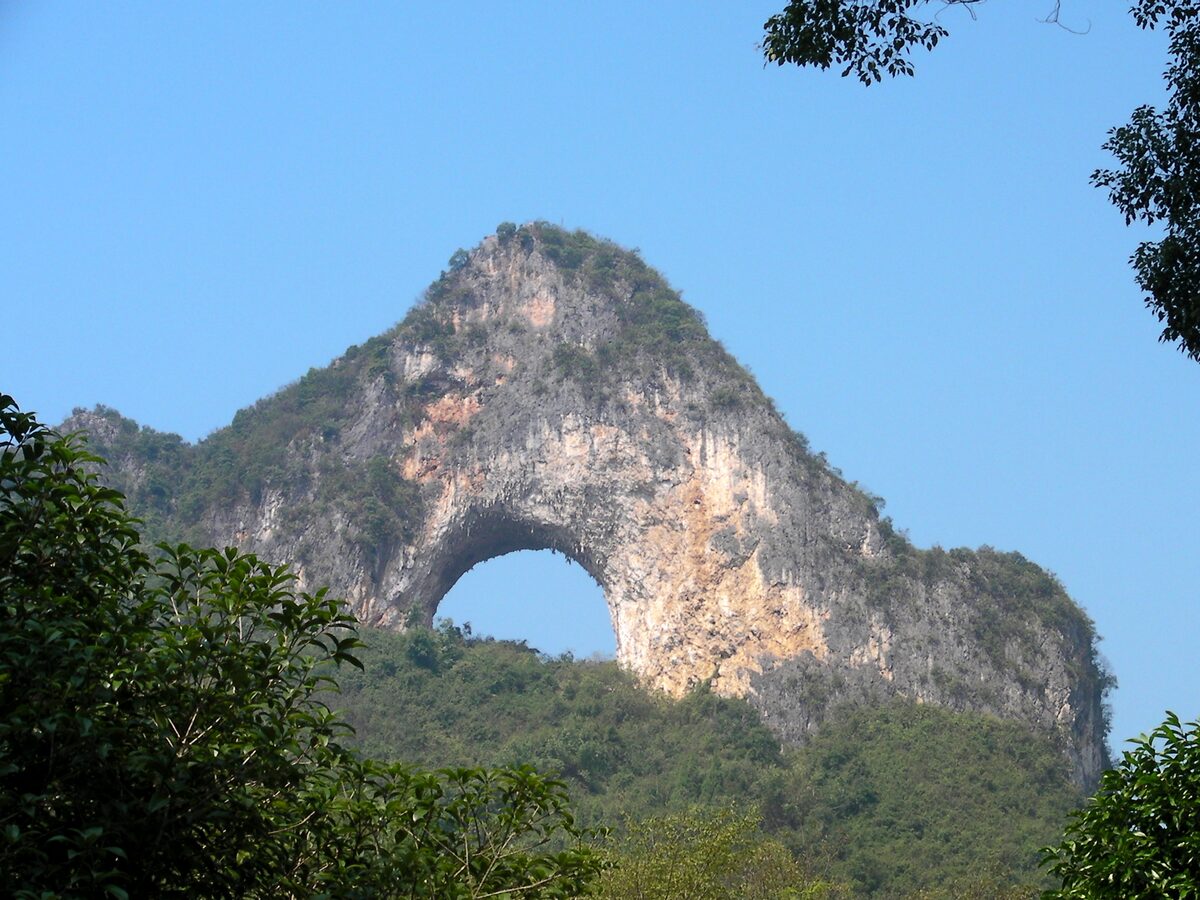 The natural arch of Moon Hill near Yangshuo framed by trees against a blue sky