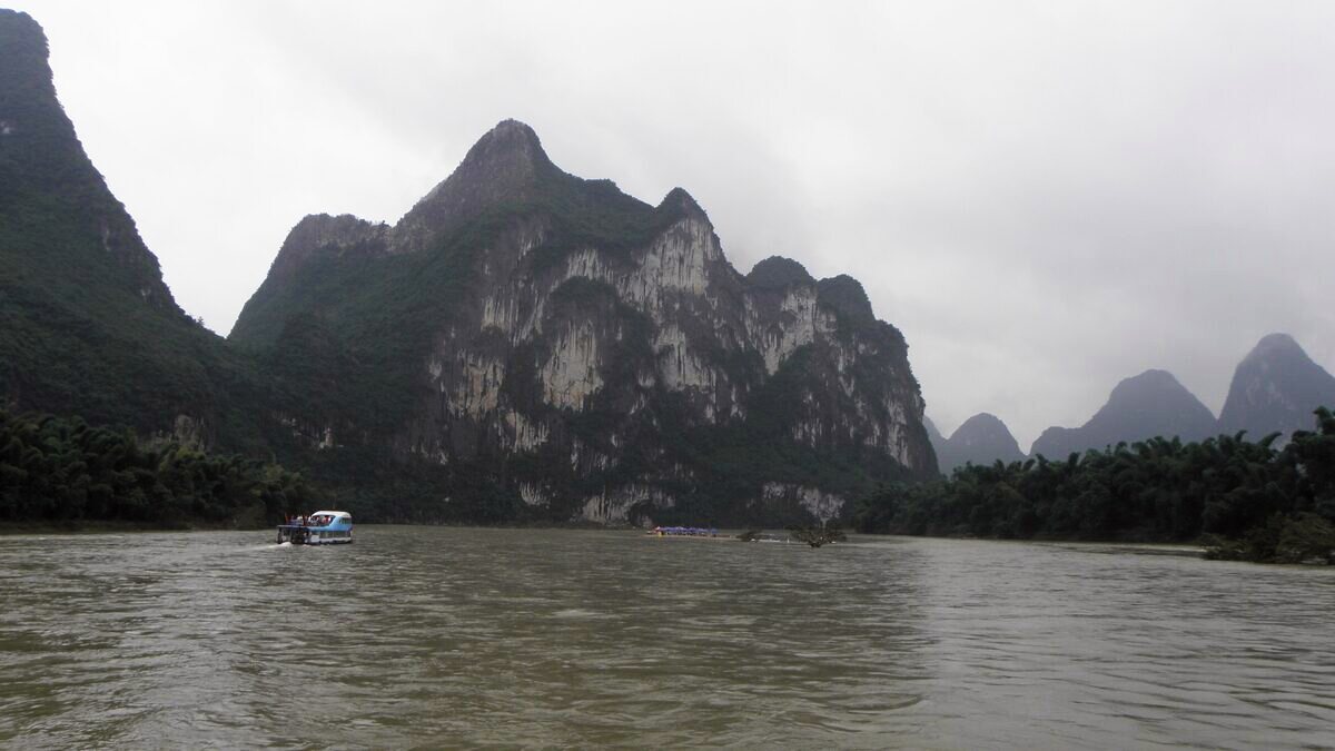 The pale limestone cliff of Nine Horse Fresco Hill rising above the Li River under an overcast sky