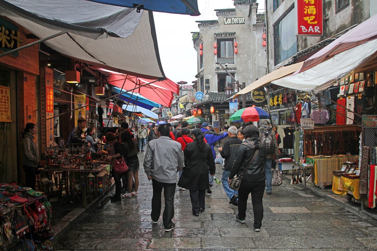 Visitors walking along West Street in Yangshuo past souvenir shops and awnings on a wet day