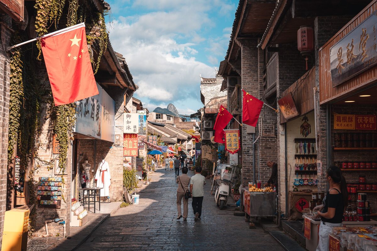 A stone-paved street of old brick shops with red flags in Xingping old town, with karst peaks at the far end