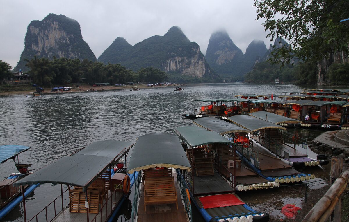 Bamboo rafts with canopies and wooden seats moored on the Li River below misty karst peaks