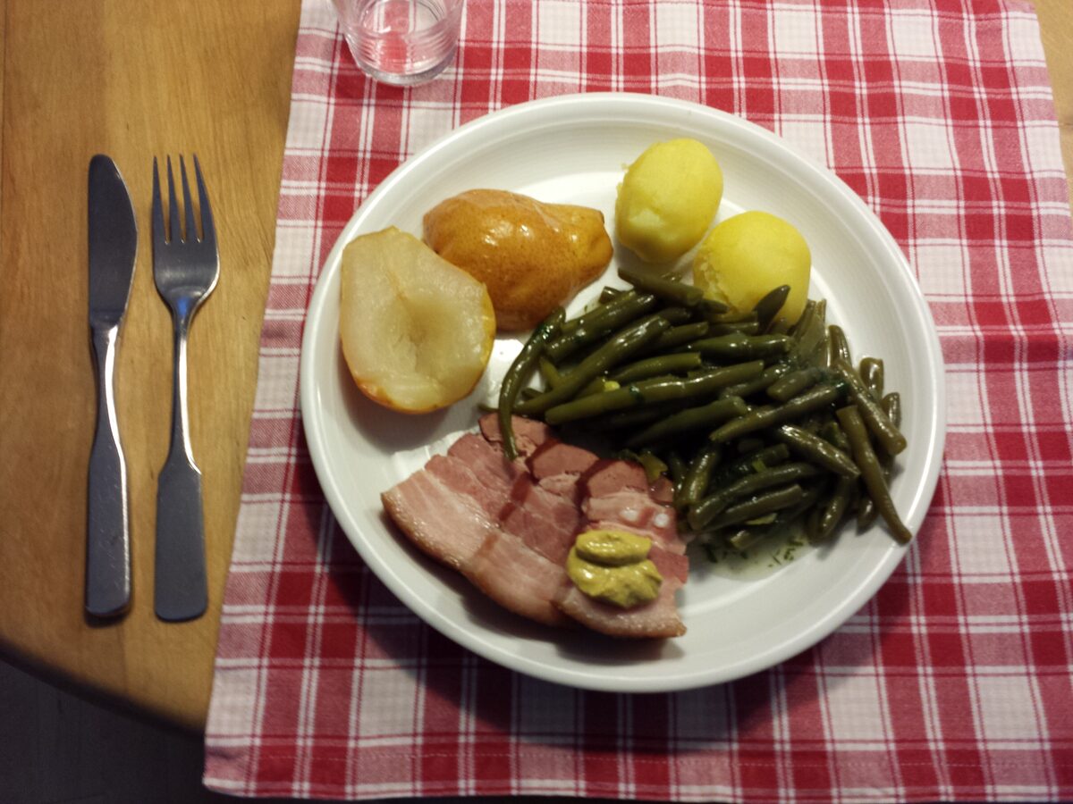 A plate of green beans, boiled potatoes, pears and a slice of bacon with mustard