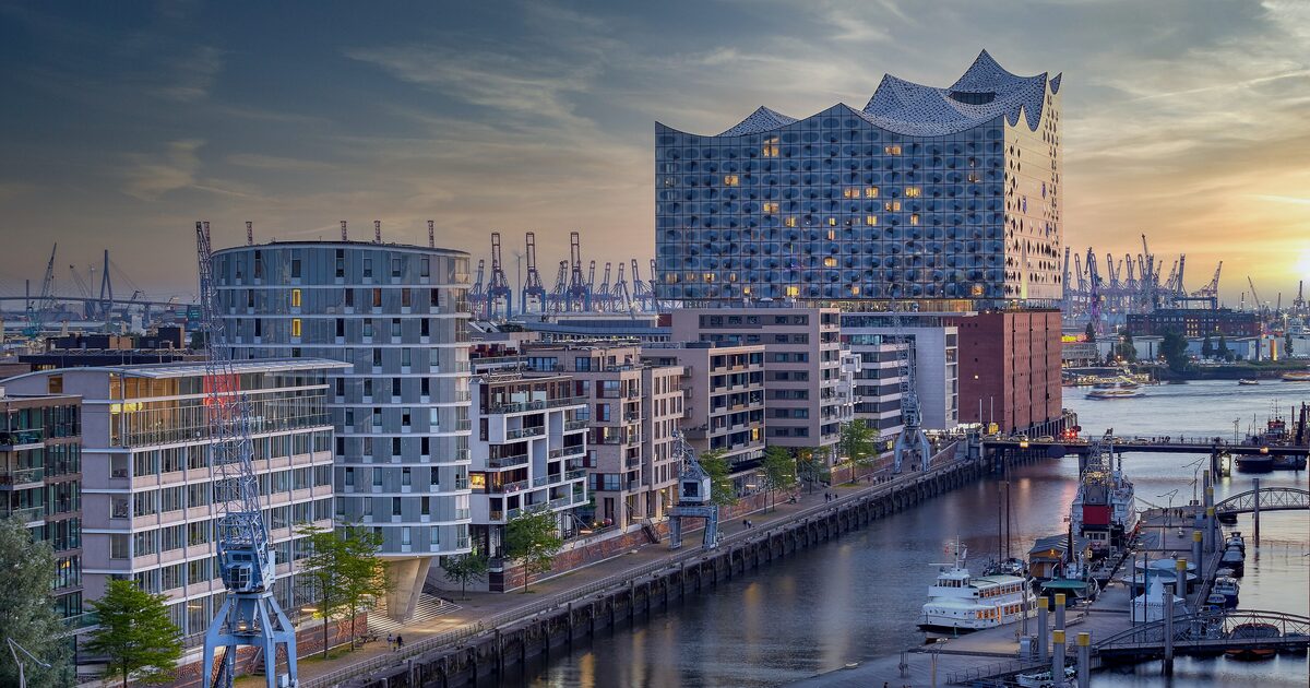 The glass wave of the Elbphilharmonie on its brick warehouse base, with harbor cranes and the Elbe in front