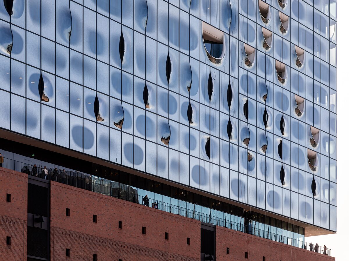 The glass facade of the Elbphilharmonie above its brick warehouse base, with visitors up on the Plaza level