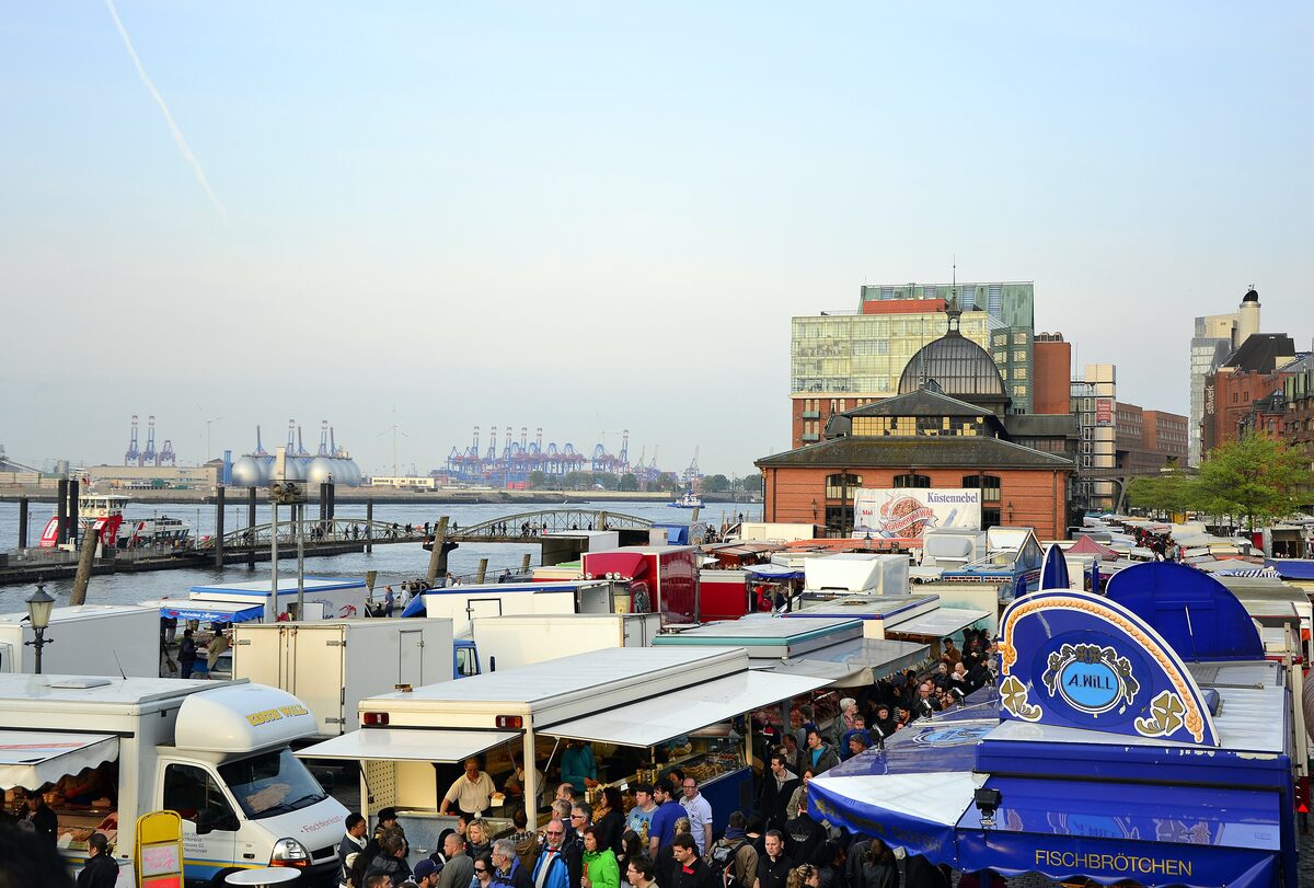 Crowds among market stalls on the Elbe at the Altona Fischmarkt, with the dome of the fish auction hall behind them