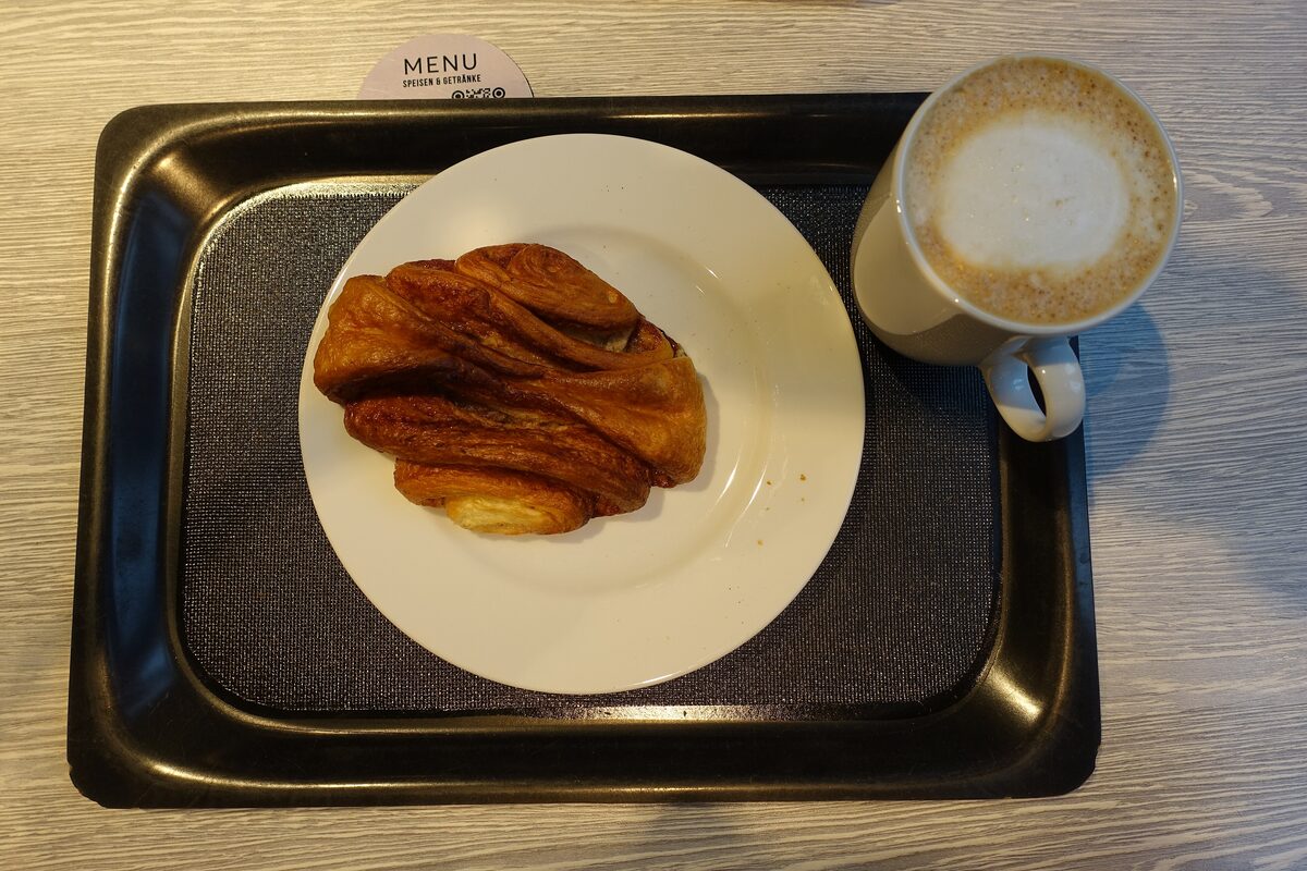 A Franzbrötchen on a plate next to a cup of milky coffee