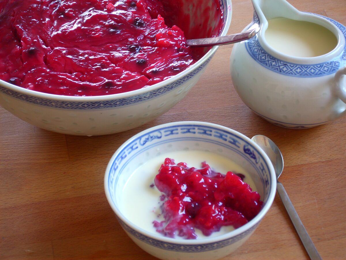 A bowl of red berry pudding with a jug of vanilla sauce beside it