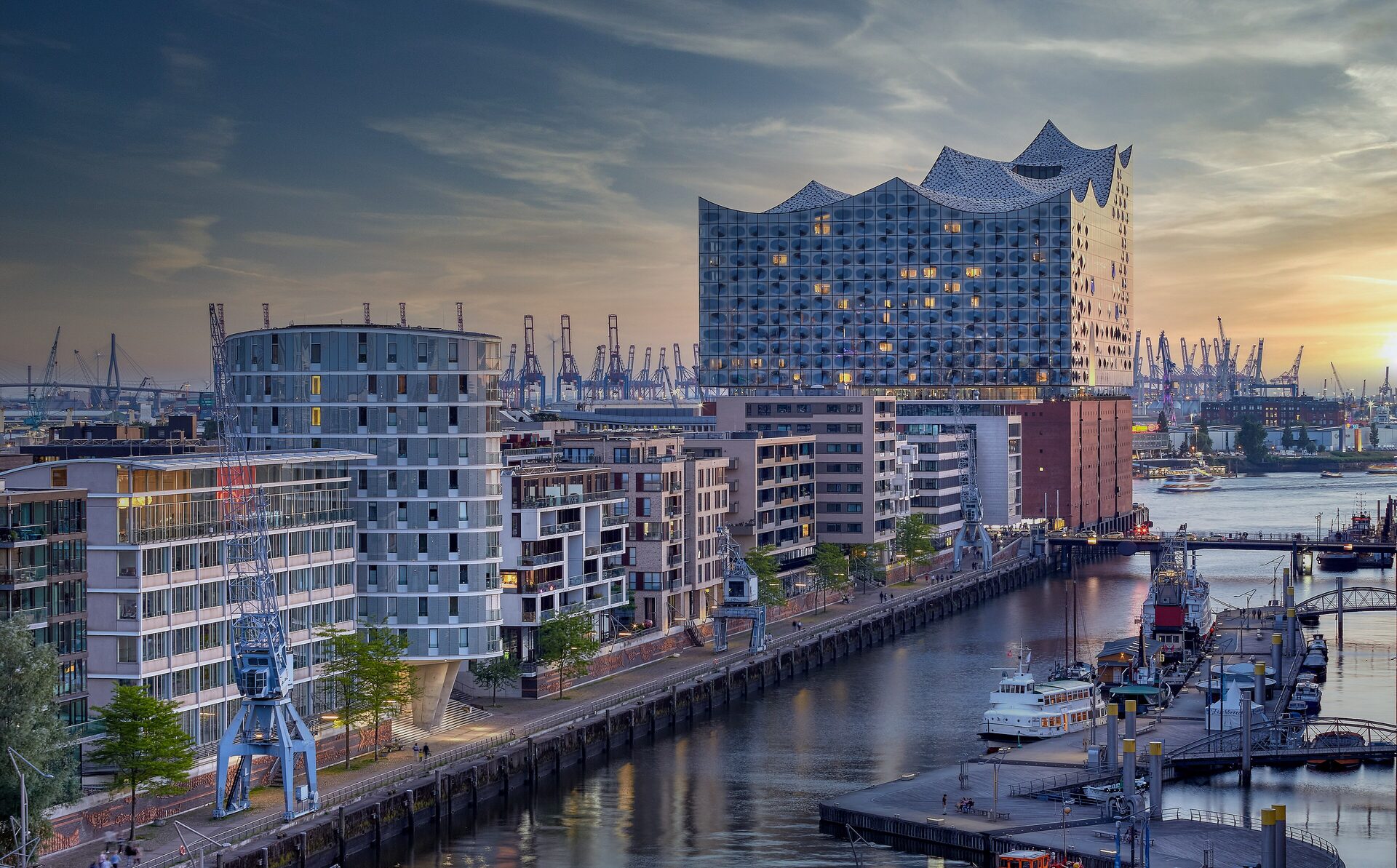 The glass wave of the Elbphilharmonie on its brick warehouse base, with harbor cranes and the Elbe in front