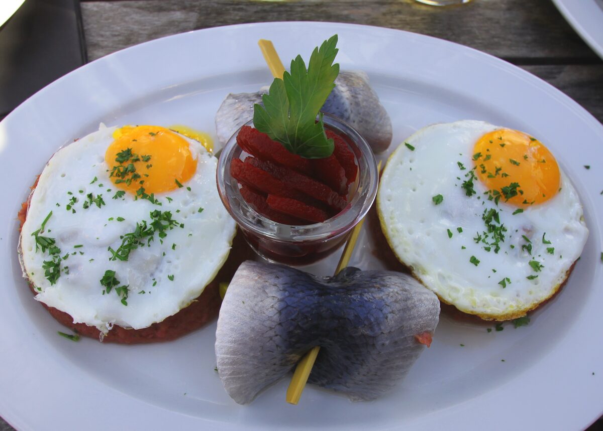 Labskaus topped with two fried eggs, with rollmops herring and a small dish of beetroot beside it