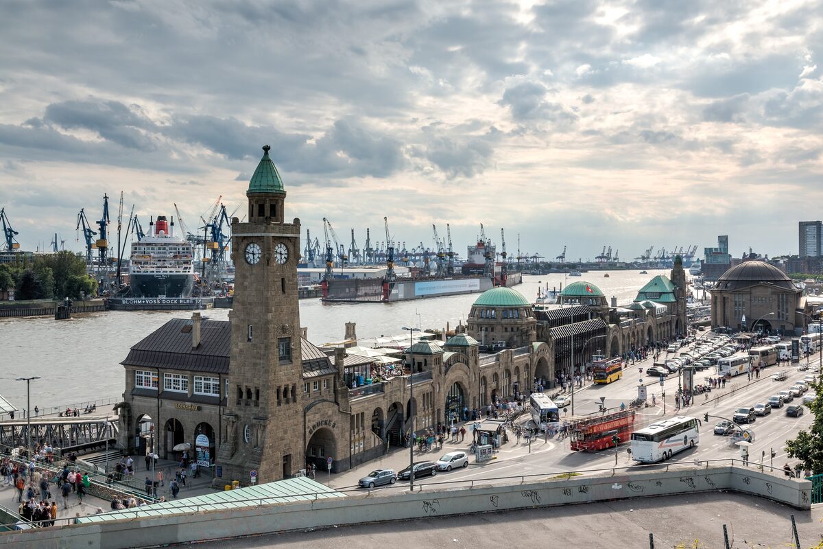 The clock tower and long pier buildings of the Landungsbrücken above the harbor, with cranes along the Elbe behind