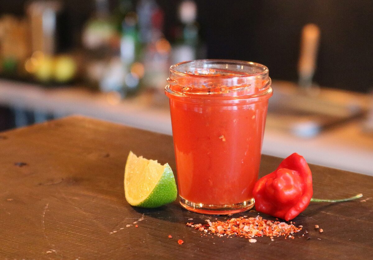 A glass of Mexikaner, the spicy tomato shot, next to a lime wedge and a red chili