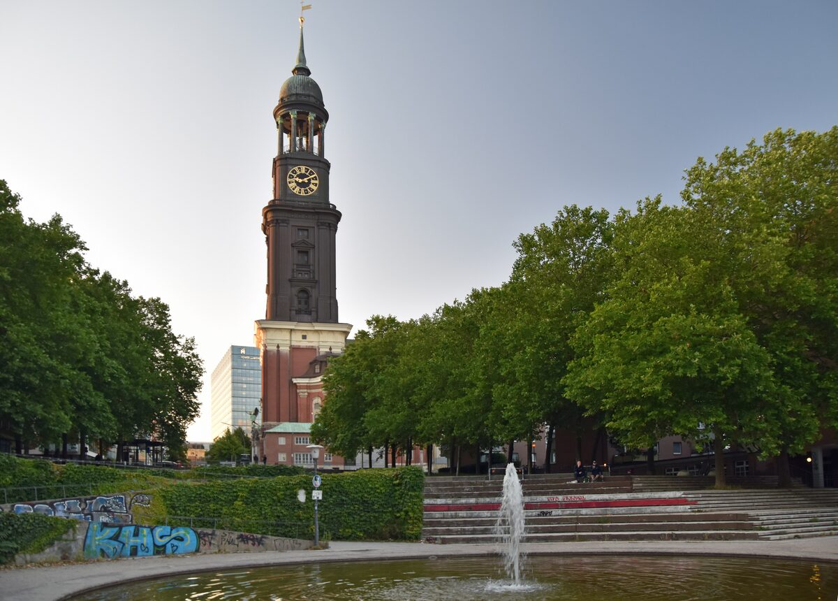 The copper-topped tower of St. Michaelis church rising above trees, with a fountain in the foreground