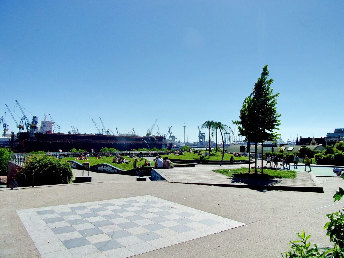 The Park Fiction terrace in St. Pauli with a giant chessboard on the paving, palm trees and harbor cranes behind