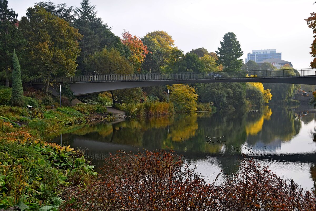 A footbridge over the lake in Planten un Blomen, with trees in autumn colors reflected in the water