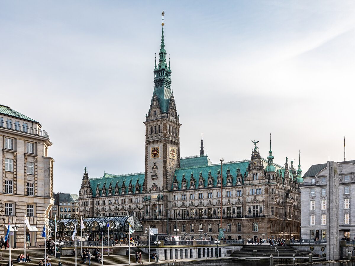 The green-roofed Hamburg town hall and its tall clock tower under a partly cloudy sky