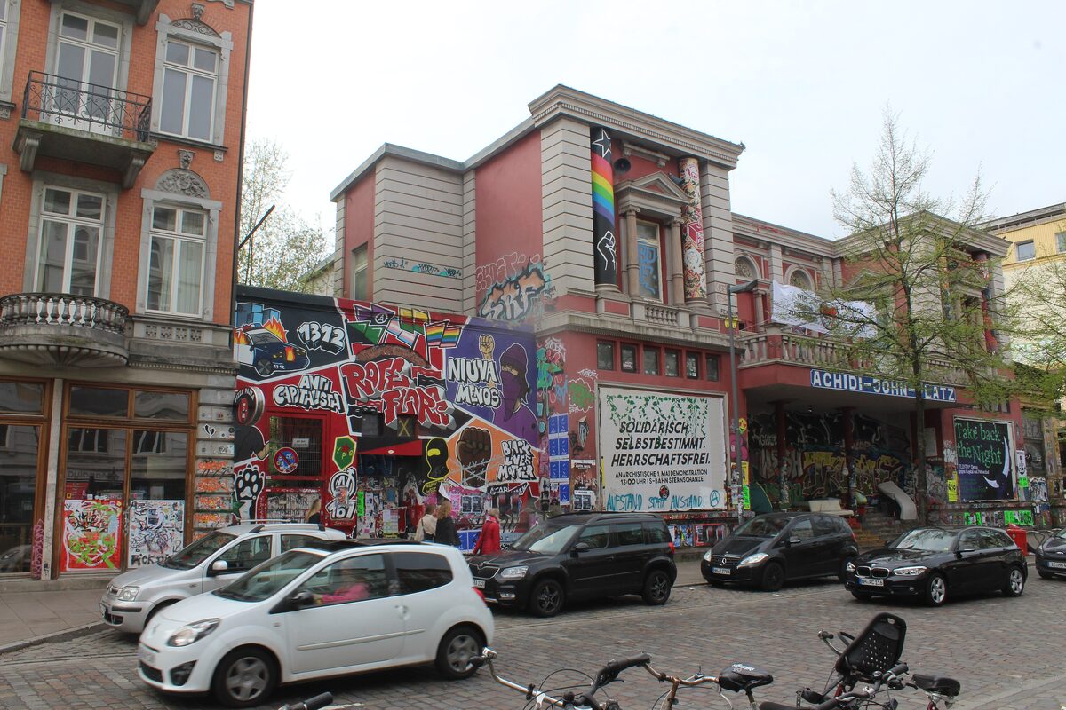 The Rote Flora on Schulterblatt, covered in graffiti and murals, with parked cars in front