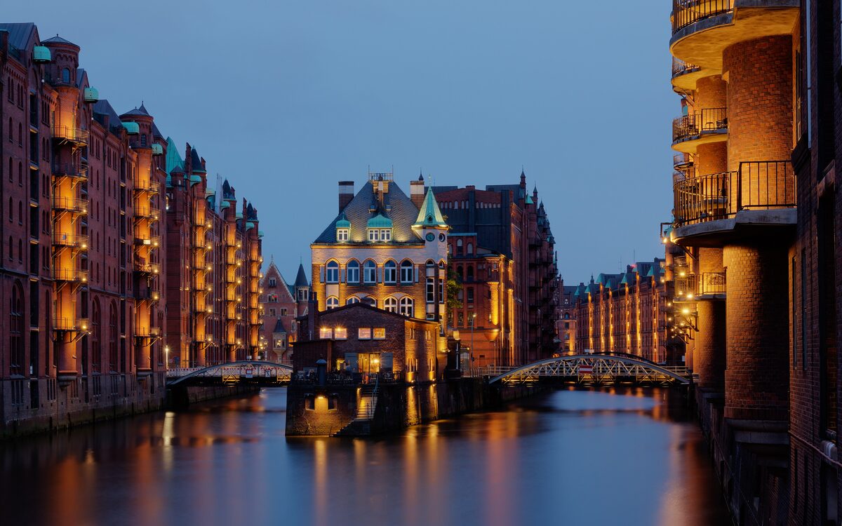 The moated Wasserschloss and brick warehouses of the Speicherstadt lit up at dusk and reflected in the canal
