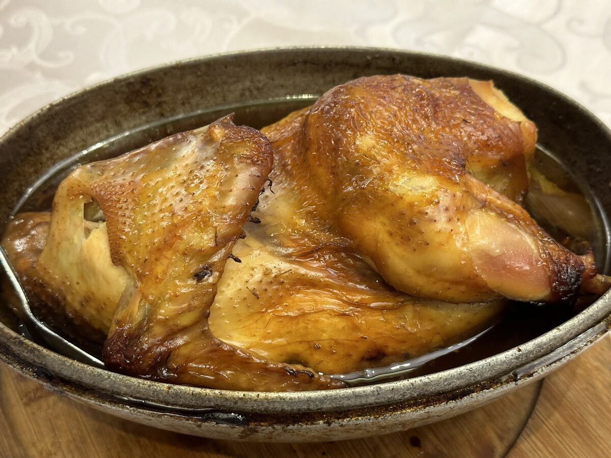 A golden-brown roasted chicken, halved and lying in a dark oval baking dish