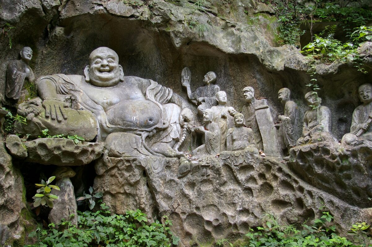 A laughing Buddha and smaller figures carved into the weathered rock face at Feilai Feng
