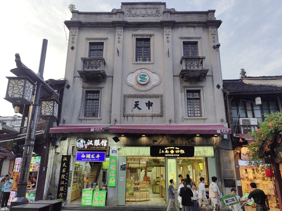 A grey Republic-era corner building with balconies above busy shops and a street lantern on Hefang Street
