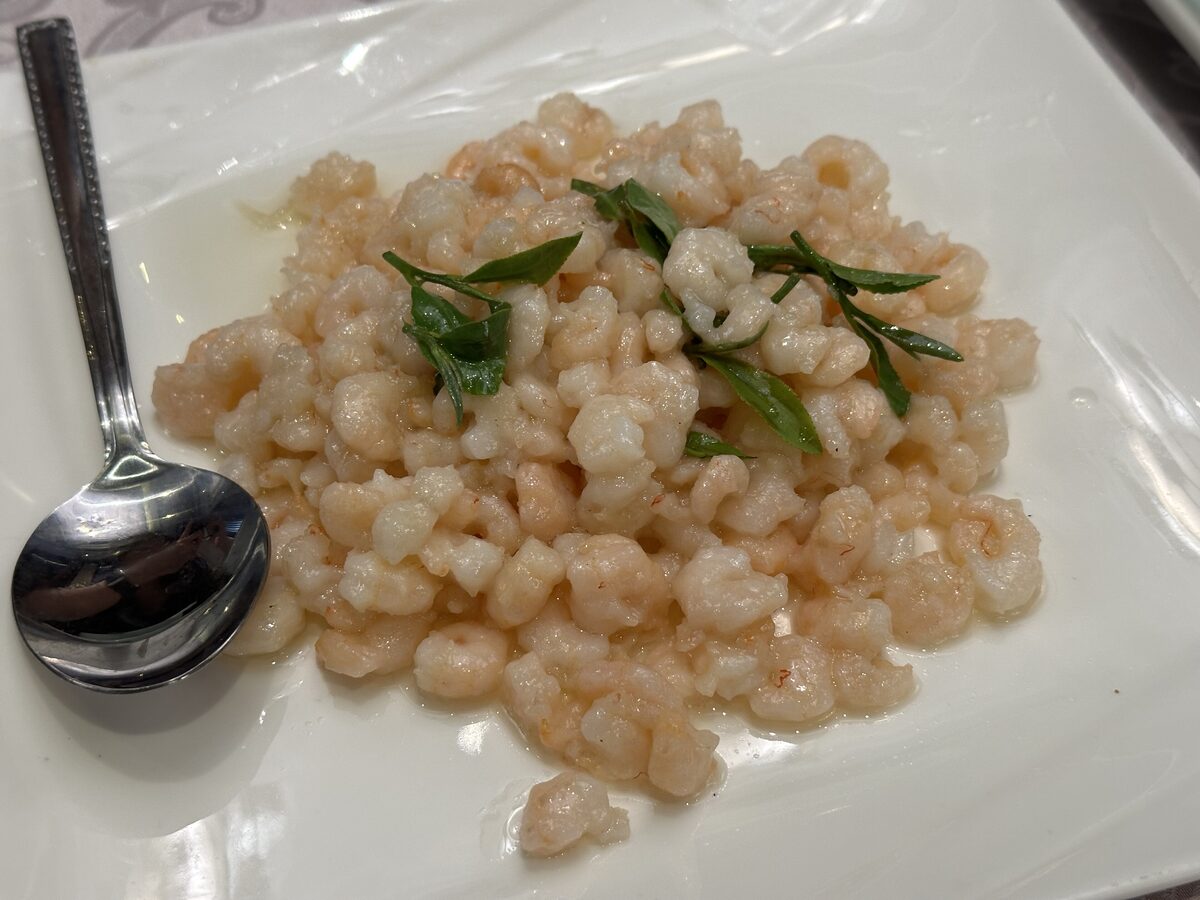 A plate of peeled shrimp stir-fried with Longjing tea leaves, with a spoon beside it