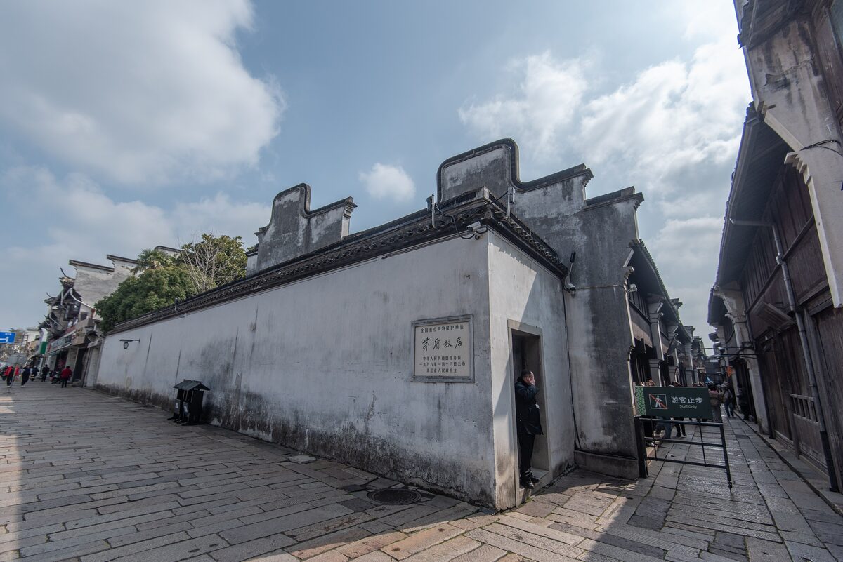 The long whitewashed wall and doorway of Mao Dun's former residence on a stone-paved Wuzhen street