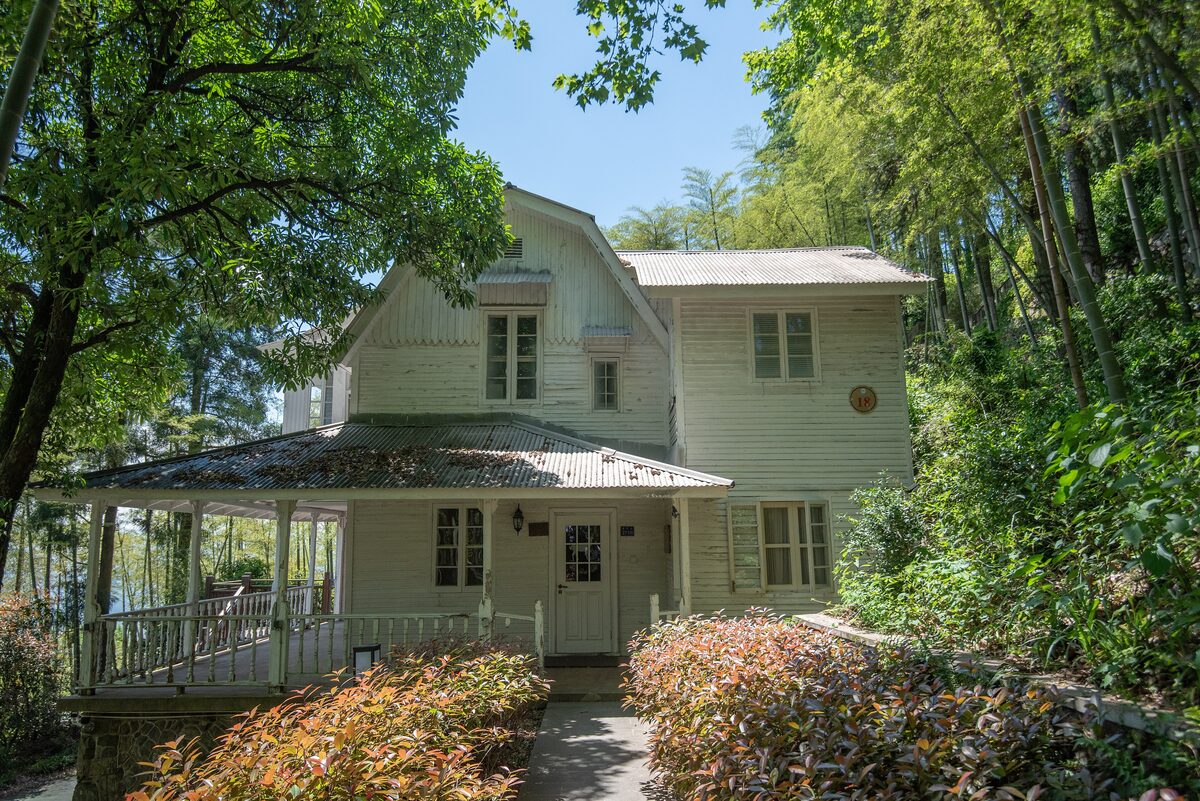 A pale timber villa with a covered porch among bamboo and trees on Moganshan
