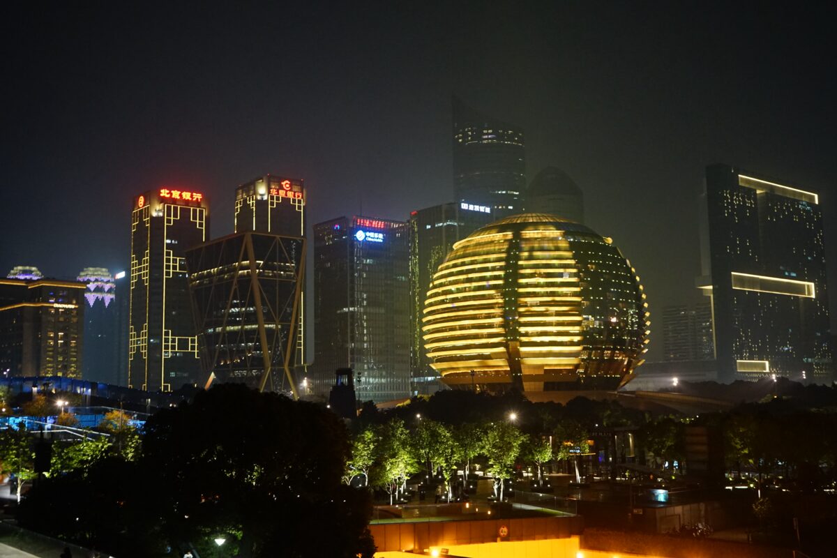 Towers of Qianjiang New City lit up at night around a glowing golden sphere-shaped building