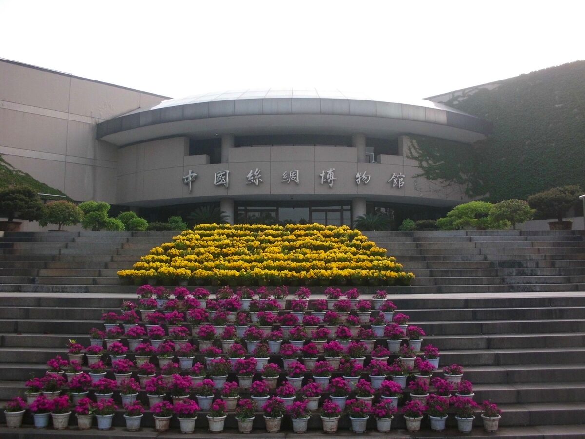 The entrance of the China National Silk Museum with its name over the door and tiers of yellow and pink flowers on the steps