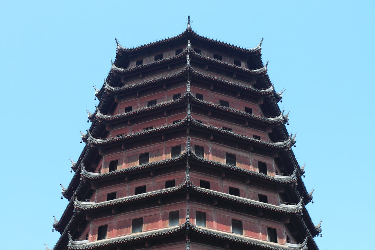 The upper tiers of Six Harmonies Pagoda, with red walls and dark curved eaves against a clear blue sky