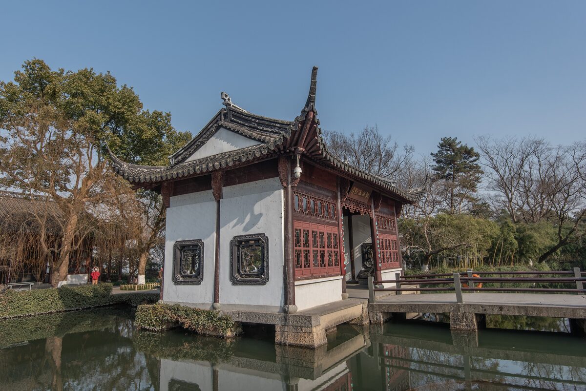 A white-walled pavilion with carved wooden windows beside a pond on Xiaoyingzhou island in West Lake