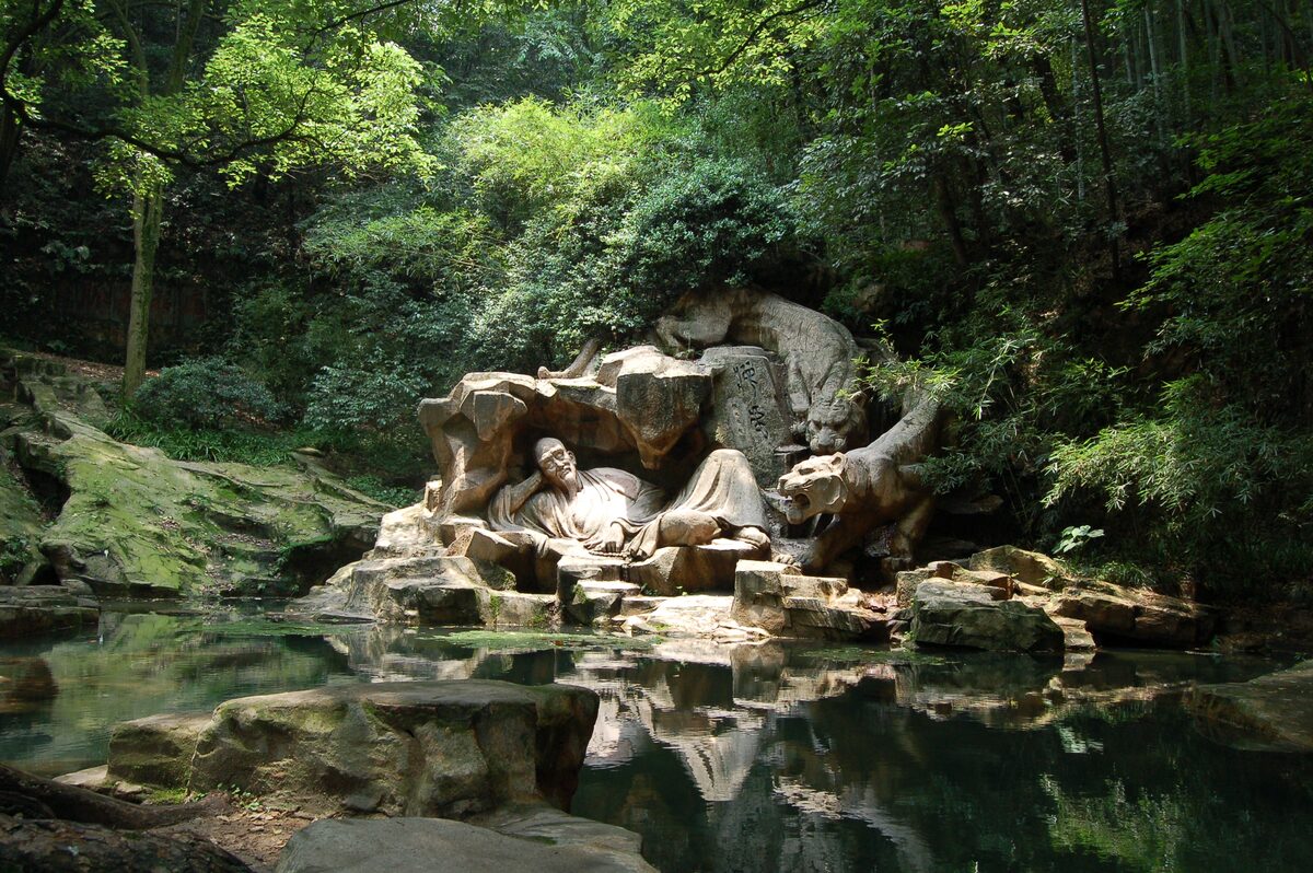 A stone sculpture of a reclining figure and a tiger beside a still pool in the woods at Tiger Spring