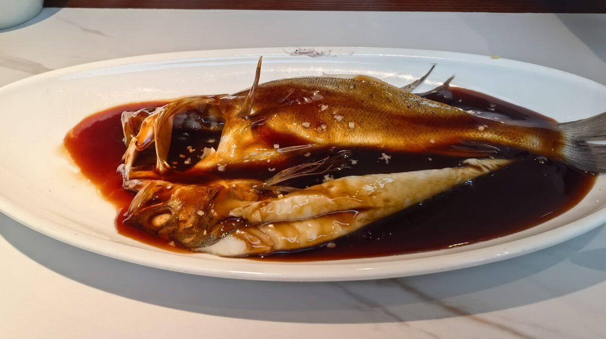 A whole fish in glossy dark vinegar sauce on a white oval plate