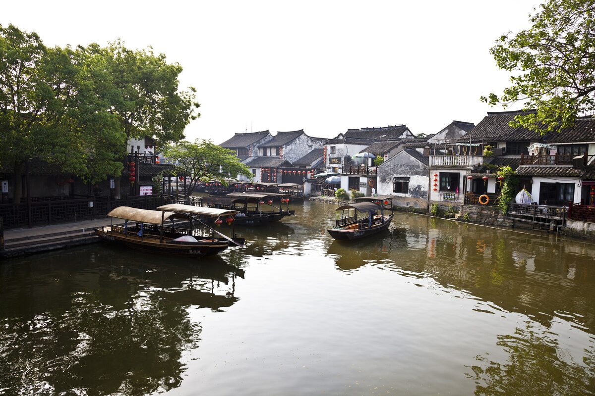 Covered tour boats moored on a canal in Xitang, with old white houses along the far bank
