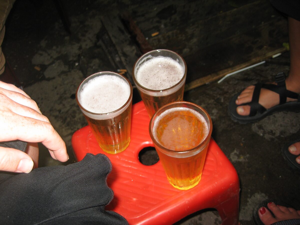 Three glasses of fresh bia hoi on a red plastic stool at night, with foam on top