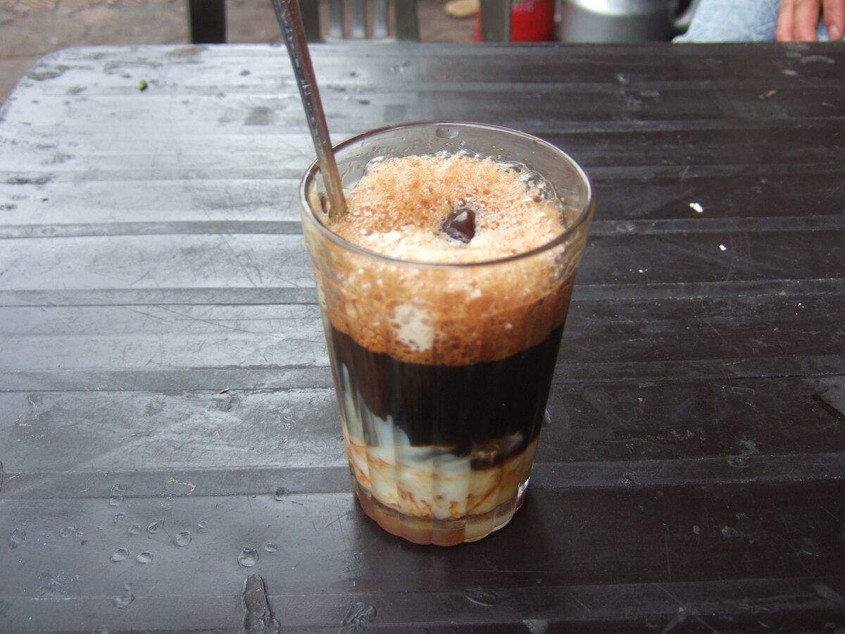 A glass of Vietnamese coffee with milk, dark coffee over condensed milk under a foamy top