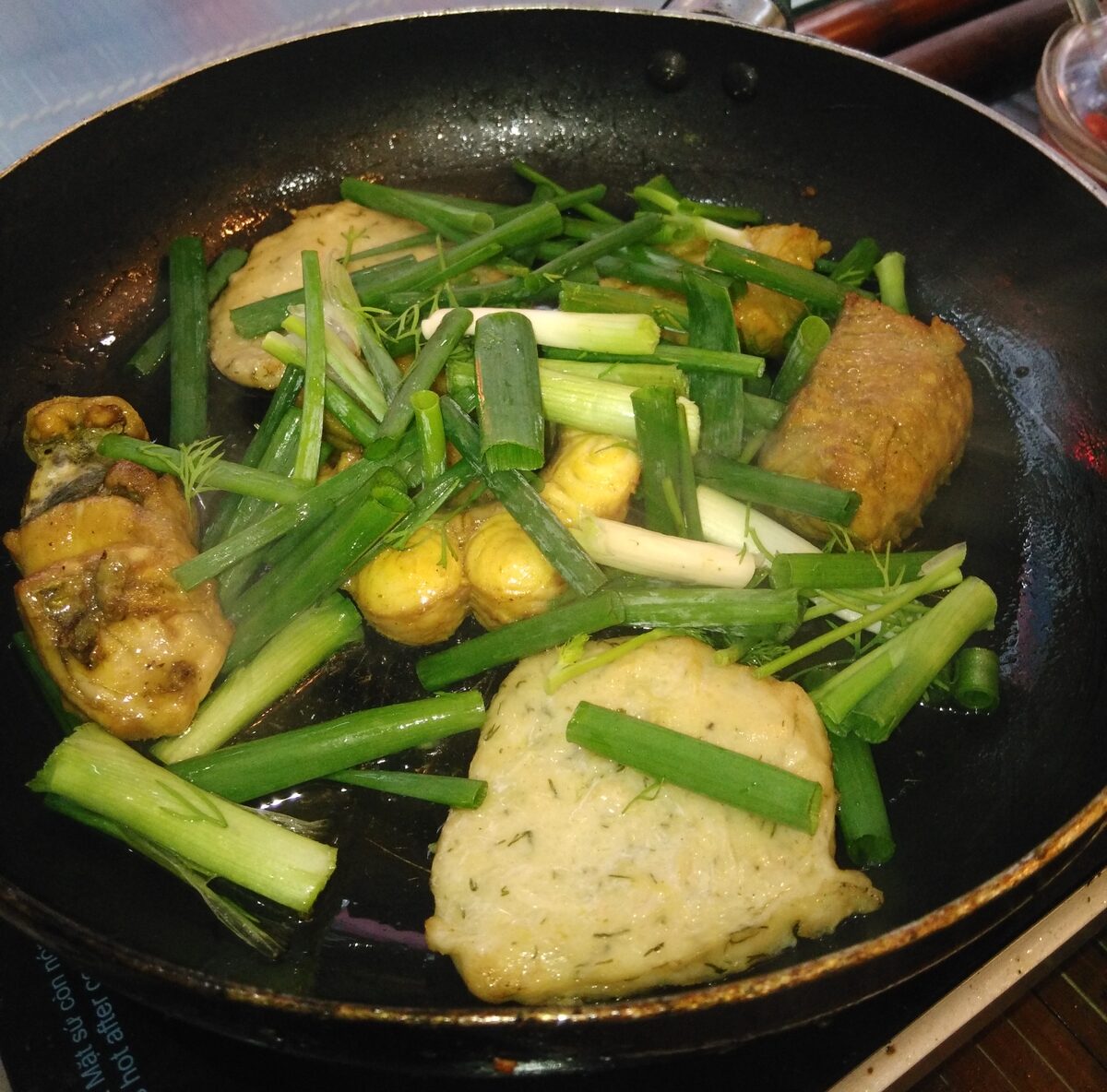 Fish pieces fried in a black pan with spring onion, the way cha ca is served