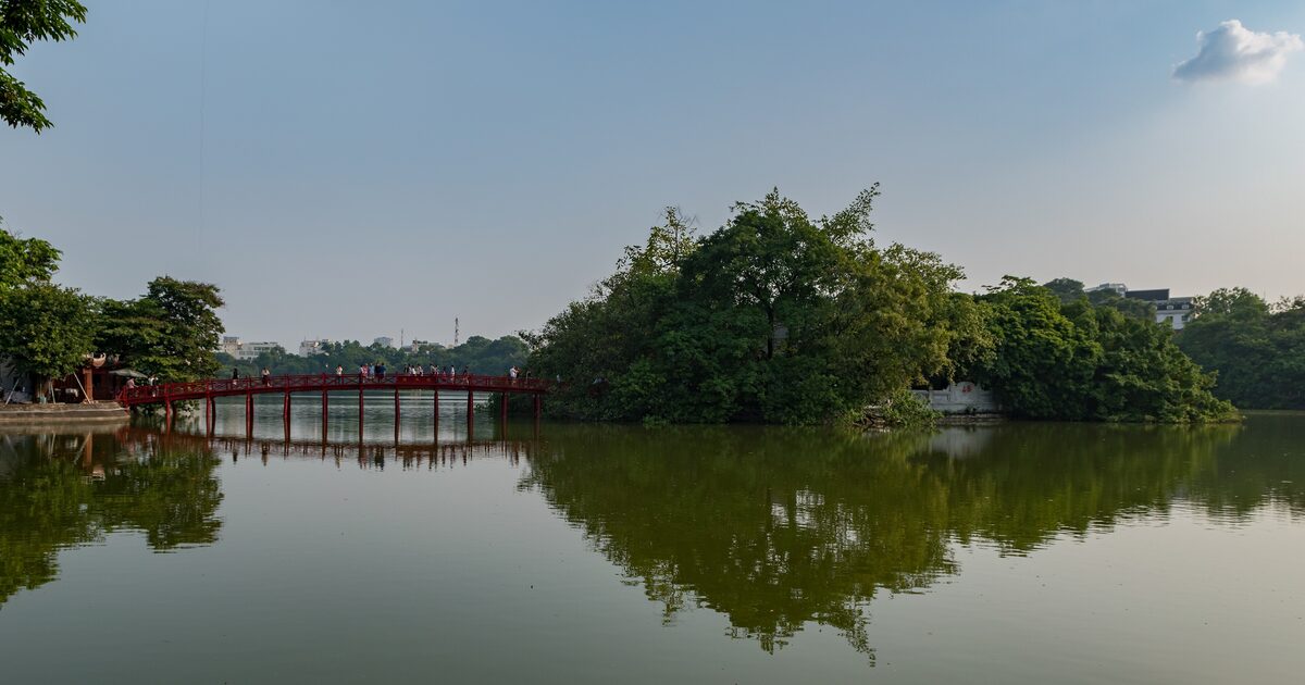 Hoan Kiem Lake under a clear blue sky, the red Huc Bridge running out to the wooded island of Ngoc Son Temple