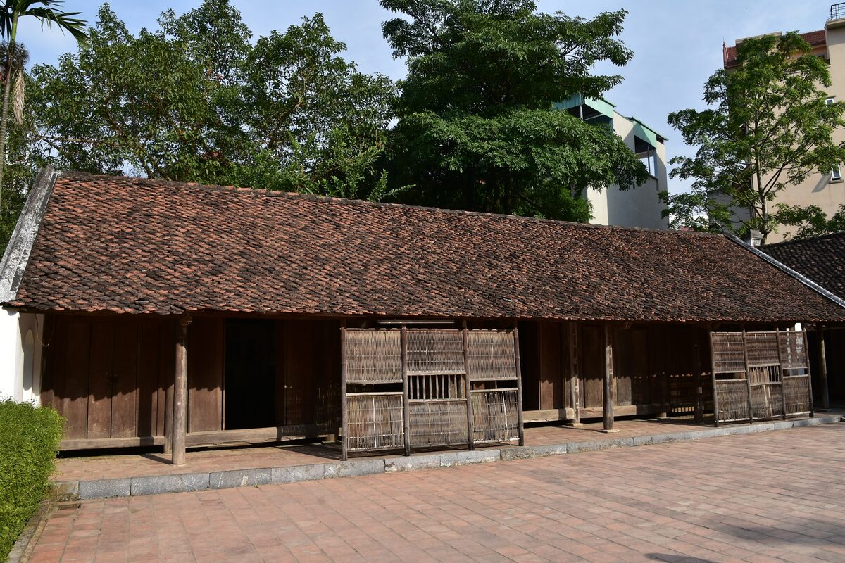 A traditional wooden house with a long tiled roof in the open-air grounds of the Vietnam Museum of Ethnology