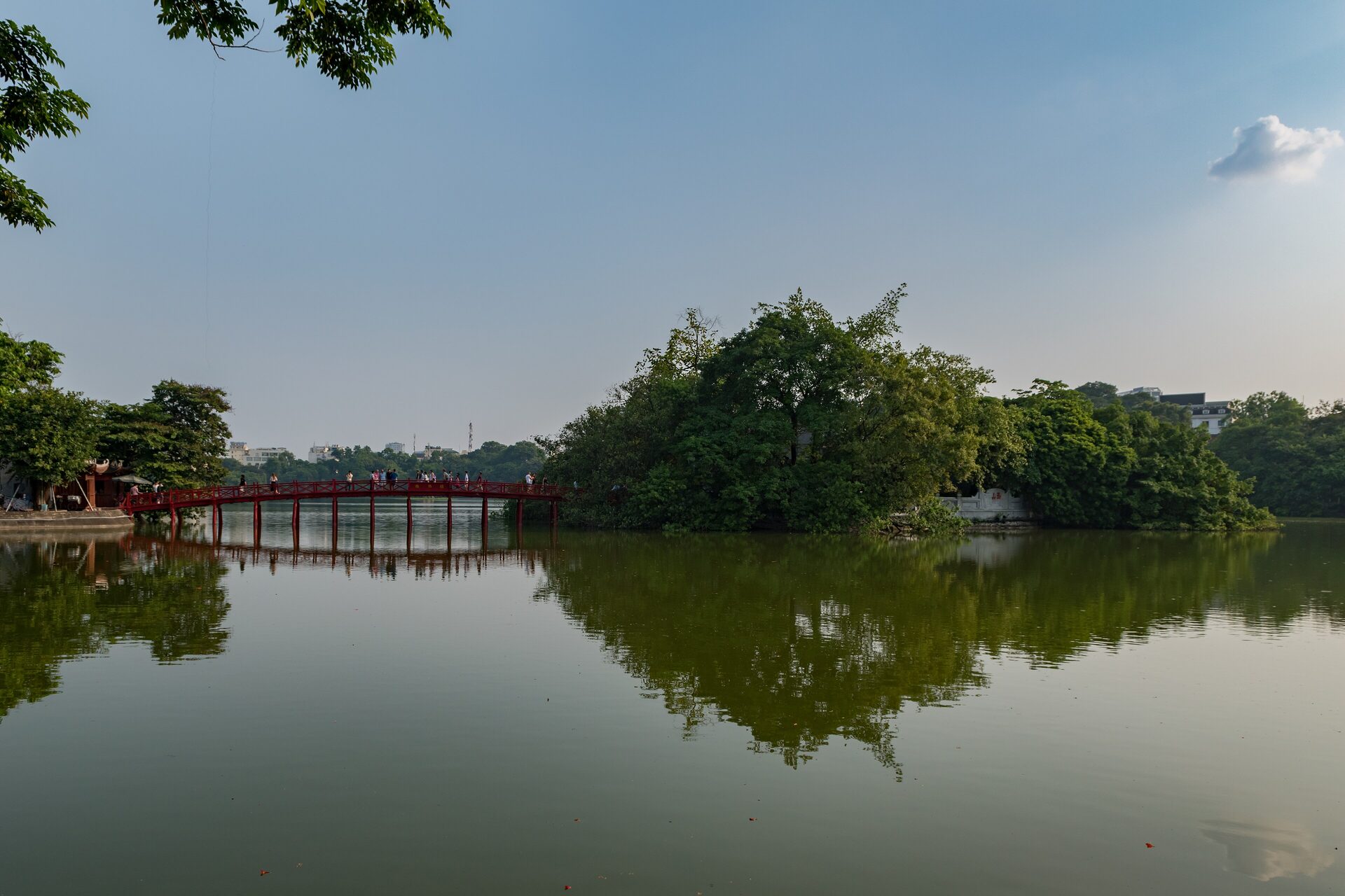 Hoan Kiem Lake under a clear blue sky, the red Huc Bridge running out to the wooded island of Ngoc Son Temple
