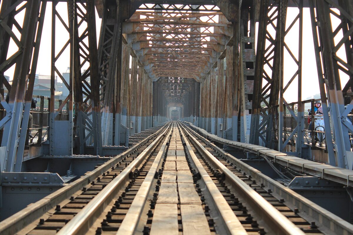 The railway track running between the steel trusses of Long Bien Bridge in afternoon light