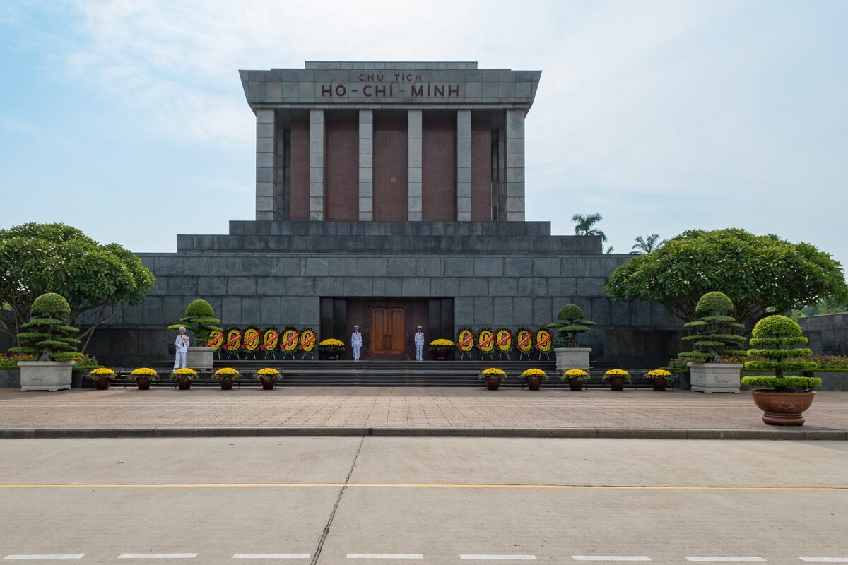 Ho Chi Minh Mausoleum, a grey granite building with a colonnade, seen across Ba Dinh Square with wreaths and two guards at its door
