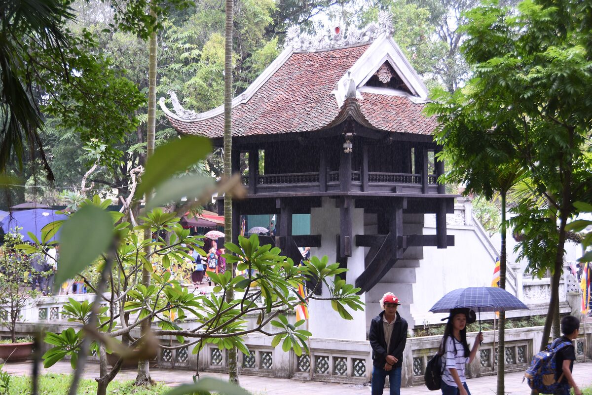 One Pillar Pagoda, a small wooden temple on a single stone pillar, with frangipani trees and visitors
