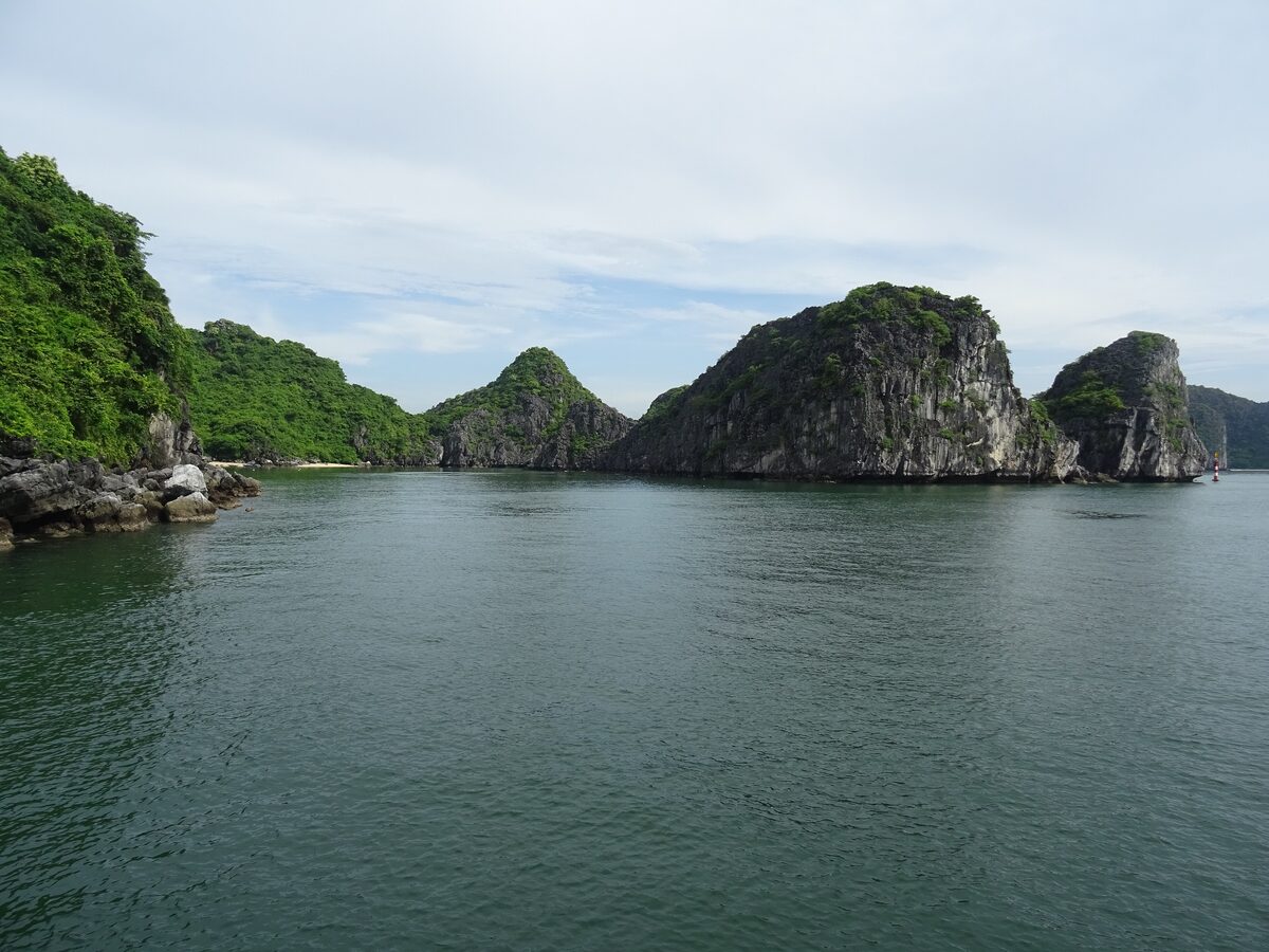 Calm green water and limestone islands in Lan Ha Bay under a pale sky