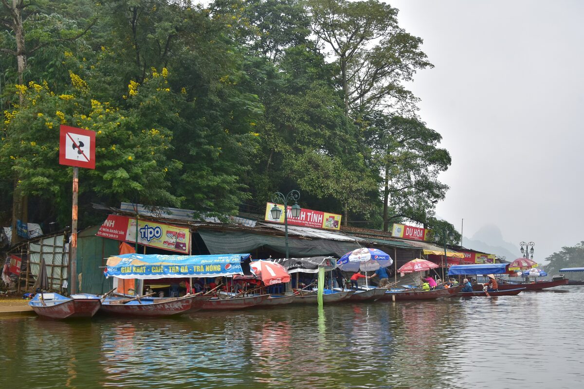 Boats and riverside stalls at the landing for the Perfume Pagoda, with wooded hills behind
