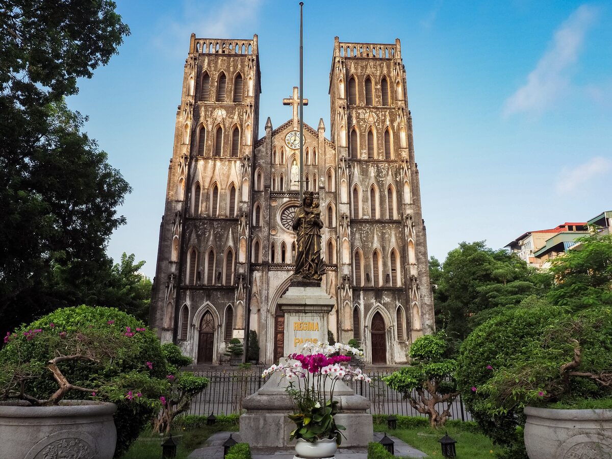 The twin Gothic towers of St. Joseph's Cathedral in daylight, with a statue and bonsai in the front garden