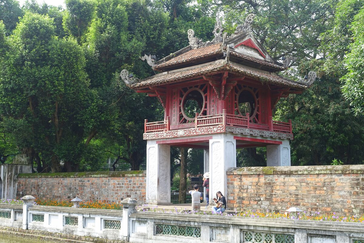 Khue Van Cac, the red and white two-story pavilion of the Temple of Literature, standing behind a brick wall among tall trees