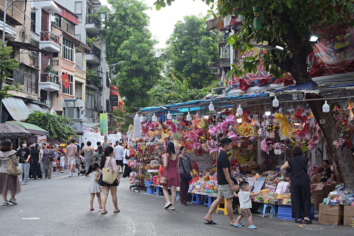 Families walking past a stall of colorful lanterns and toys on a busy street in Hanoi