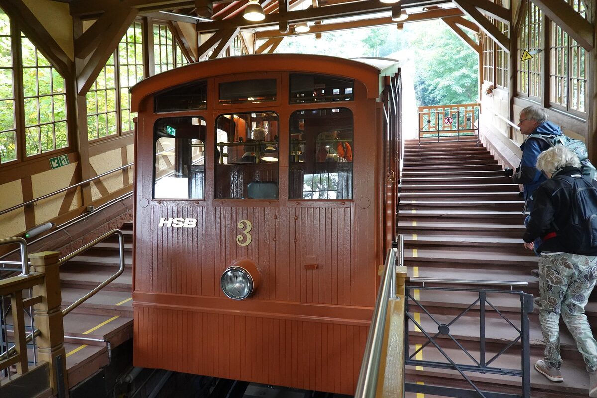 The wooden funicular car of the Heidelberg Bergbahn at its station, with passengers climbing the stairs beside it
