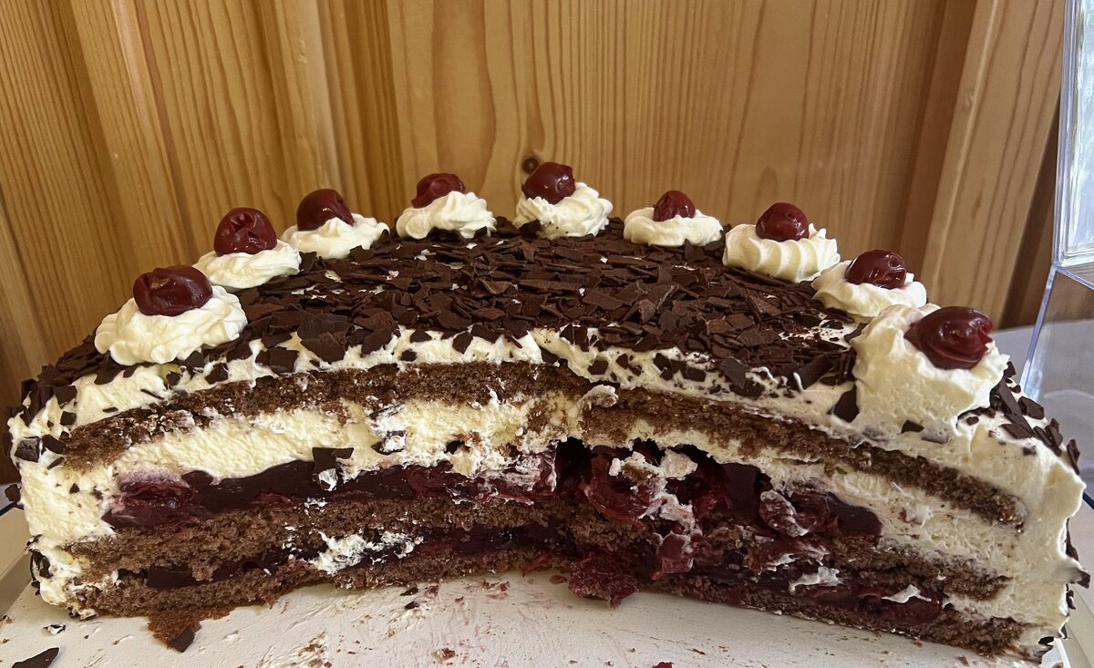 A Black Forest cake cut open to show layers of sponge, cream and cherries under chocolate shavings